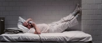 Movie still from “Manhunter” (1986), directed by Michael Mann – A man laying on a bed talking on a phone; Wide shot, Overhead angle