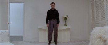 Movie still from “Manhunter” (1986), directed by Michael Mann – A man standing in front of a table with a vase of flowers in it; Wide shot, Low angle