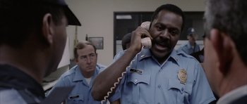 Movie still from “Manhunter” (1986), directed by Michael Mann – A man holding a phone up to his ear while standing next to another man; Close Up shot, Low angle