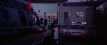 Movie still from “Manhunter” (1986), directed by Michael Mann – A woman standing in front of a police car; Wide shot, Low angle