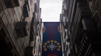 Movie still from “Maquia: When the Promised Flower Blooms” (2018), directed by Jong Heo – A blue and yellow banner hanging from a building; Extreme Wide shot, Low angle