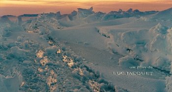 Movie still from “March of the Penguins” (2005), directed by Luc Jacquet – A view of a snowy field with a sunset in the background; Extreme Wide shot, High angle