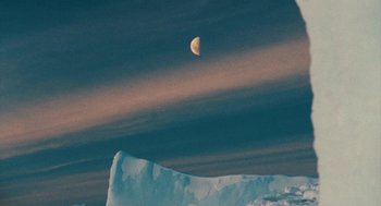 Movie still from “March of the Penguins” (2005), directed by Luc Jacquet – The moon is setting in the dark sky over a large block of ice; Extreme Wide shot, Low angle