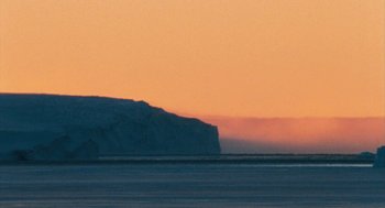 Movie still from “March of the Penguins” (2005), directed by Luc Jacquet – A view of the ocean at sunset with a mountain in the background; Extreme Wide shot, Low angle