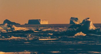 Movie still from “March of the Penguins” (2005), directed by Luc Jacquet – Two icebergs in the middle of the ocean at sunset; Extreme Wide shot, High angle