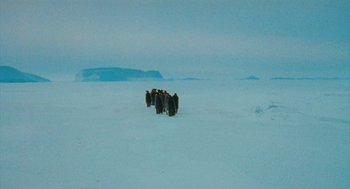 Movie still from “March of the Penguins” (2005), directed by Luc Jacquet – A group of people walking across a snow covered field; Extreme Wide shot, High angle