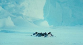 Movie still from “March of the Penguins” (2005), directed by Luc Jacquet – A group of penguins laying in the snow together; Extreme Wide shot, High angle