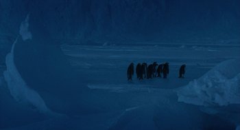 Movie still from “March of the Penguins” (2005), directed by Luc Jacquet – A group of penguins standing on top of a snow covered ground; Extreme Wide shot, High angle