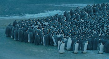 Movie still from “March of the Penguins” (2005), directed by Luc Jacquet – A large group of penguins gathered together on the beach; Extreme Wide shot, High angle