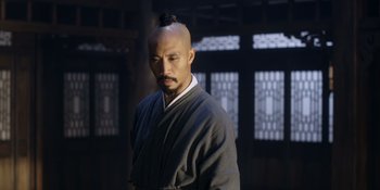 Movie still from “Marco Polo” (2014), created by John Fusco – A man with a shaved head is standing in front of a window; Medium shot, Over the shoulder angle