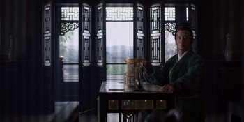 Movie still from “Marco Polo” (2014), created by John Fusco – A man sitting at a table in front of a window; Medium shot, Low angle
