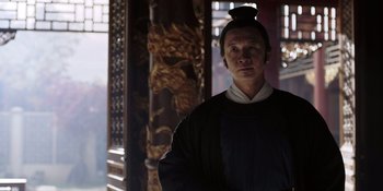 Movie still from “Marco Polo” (2014), created by John Fusco – A man in a black shirt is standing in front of a wooden pillar; Medium shot, Low angle