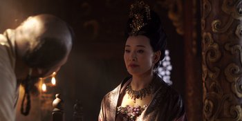 Movie still from “Marco Polo” (2014), created by John Fusco – A woman wearing a gold headpiece and a brown dress; Close Up shot, Over the shoulder angle