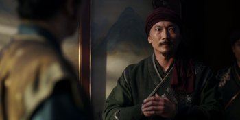 Movie still from “Marco Polo” (2014), created by John Fusco – A man with a pipe in his mouth and wearing a turban; Medium shot, Over the shoulder angle
