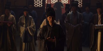 Movie still from “Marco Polo” (2014), created by John Fusco – An old man in a black hat is standing in front of a group of people; Medium shot, Low angle