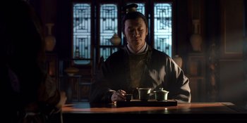 Movie still from “Marco Polo” (2014), created by John Fusco – A man sitting at a table with a tray of tea; Medium shot, Low angle
