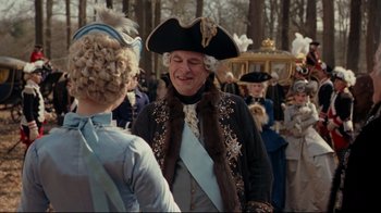 Movie still from “Marie Antoinette” (2006), directed by Sofia Coppola – A man in a hat and a fur coat talking to a woman in a dress; Medium shot, Over the shoulder angle