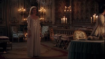 Movie still from “Marie Antoinette” (2006), directed by Sofia Coppola – A woman standing in front of a fireplace in a room; Wide shot, High angle