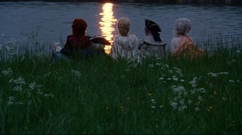Movie still from “Marie Antoinette” (2006), directed by Sofia Coppola – A group of people sitting in the grass near a body of water; Wide shot, High angle