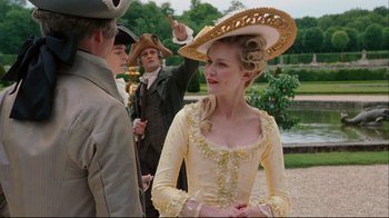 Movie still from “Marie Antoinette” (2006), directed by Sofia Coppola – A woman in a yellow dress wearing a straw hat; Medium shot, Over the shoulder angle