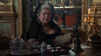 Movie still from “Marie Antoinette” (2006), directed by Sofia Coppola – An older woman sitting at a table reading a letter; Medium shot, Over the shoulder angle