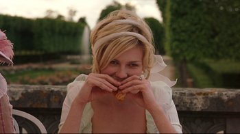 Movie still from “Marie Antoinette” (2006), directed by Sofia Coppola – A beautiful young blond haired woman biting into a pastry; Medium shot, Over the shoulder angle