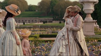 Movie still from “Marie Antoinette” (2006), directed by Sofia Coppola – A man and a woman dressed in period clothing kissing in front of a girl in a garden; Wide shot, Over the shoulder angle