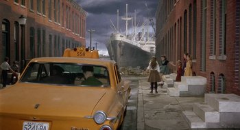 Movie still from “Marnie” (1964), directed by Alfred Hitchcock – A yellow taxi driving down a street past a large ship; Extreme Wide shot, High angle