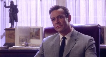 Movie still from “Marnie” (1964), directed by Alfred Hitchcock – A man wearing a suit and tie sitting in a chair; Close Up shot, Low angle