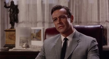 Movie still from “Marnie” (1964), directed by Alfred Hitchcock – A man wearing a suit and tie sitting in a chair; Close Up shot, Low angle
