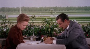 Movie still from “Marnie” (1964), directed by Alfred Hitchcock – A man and a woman sitting at a table writing on papers; Medium shot, Over the shoulder angle