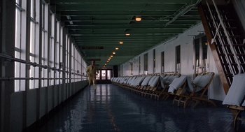 Movie still from “Marnie” (1964), directed by Alfred Hitchcock – A man walking down a long hallway with rows of lawn chairs; Wide shot, High angle