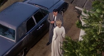 Movie still from “Marnie” (1964), directed by Alfred Hitchcock – A man and a woman standing in front of a car; Wide shot, High angle