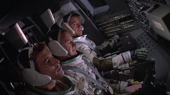 Movie still from “Marooned” (1969), directed by John Sturges – A group of men sitting next to each other in space suits; Medium shot, High angle