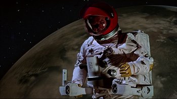 Movie still from “Marooned” (1969), directed by John Sturges – A man in a spacesuit and helmet standing next to a moon; Medium shot, Low angle