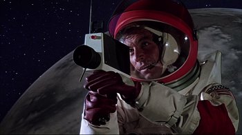 Movie still from “Marooned” (1969), directed by John Sturges – A man in a space suit holding a video camera; Medium shot, Low angle