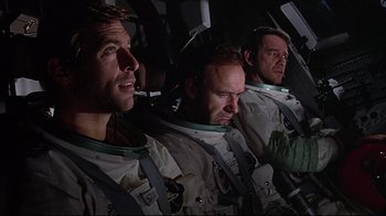 Movie still from “Marooned” (1969), directed by John Sturges – Three men in space suits are sitting in the cockpit of an airplane; Medium shot, Low angle