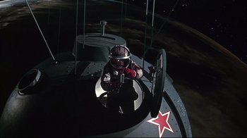 Movie still from “Marooned” (1969), directed by John Sturges – A man in a red helmet is inside of an airplane; Wide shot, Low angle