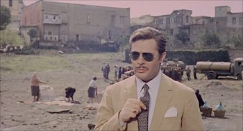 Movie still from “Marriage Italian Style” (1964), directed by Vittorio De Sica – A man wearing a suit and tie standing on a beach; Medium shot, Over the shoulder angle