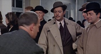Movie still from “Marriage Italian Style” (1964), directed by Vittorio De Sica – A man in a trench coat and a hat is talking to another man in a suit and tie; Medium shot, Over the shoulder angle