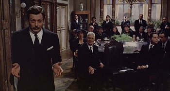Movie still from “Marriage Italian Style” (1964), directed by Vittorio De Sica – A group of people in suits sitting in a living room; Medium shot, Over the shoulder angle