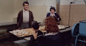 Movie still from “Marriage Italian Style” (1964), directed by Vittorio De Sica – A group of people standing around a table filled with donuts; Medium shot, Over the shoulder angle