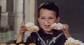 Movie still from “Marriage Italian Style” (1964), directed by Vittorio De Sica – A young boy holding two doughnuts in front of his face; Medium shot, High angle