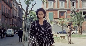 Movie still from “Marriage Italian Style” (1964), directed by Vittorio De Sica – A woman in a polka dot dress standing on the sidewalk; Wide shot, Low angle