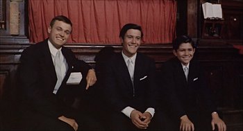 Movie still from “Marriage Italian Style” (1964), directed by Vittorio De Sica – Three young men in suits sitting next to each other in front of a red curtain; Medium shot, High angle