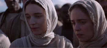 Movie still from “Mary Magdalene” (2018), directed by Garth Davis – Two women are standing in front of a group of people; Close Up shot, Over the shoulder angle