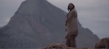 Movie still from “Mary Magdalene” (2018), directed by Garth Davis – A man standing on top of a mountain covered in a blanket; Medium shot, Low angle