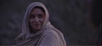 Movie still from “Mary Magdalene” (2018), directed by Garth Davis – A woman wearing a headscarf is smiling for the camera; Close Up shot, Over the shoulder angle