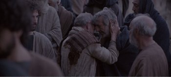 Movie still from “Mary Magdalene” (2018), directed by Garth Davis – Two older men embracing each other in a crowd; Medium shot, Over the shoulder angle