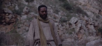 Movie still from “Mary Magdalene” (2018), directed by Garth Davis – A man wearing a robe and scarf standing in front of a cliff; Medium shot, Low angle